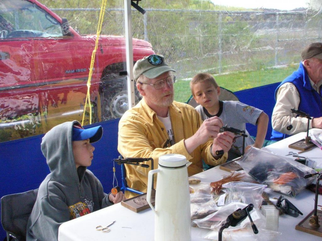 photo of a man tying flies while two children look on