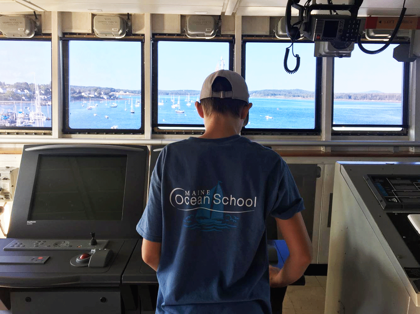 a teenager at the helm of a boat wearing a Maine Ocean School t-shirt