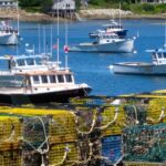 lobster boat in water behind stacked traps on shore