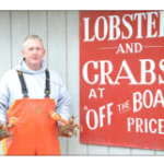 lobsterman holding a lobster in each hand in front of a sign reading 'Lobster and Crabs at "off the boat" prices'