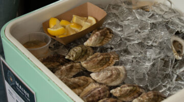 Oysters on a half-shell, on ice and a brown container with lemon wedges.