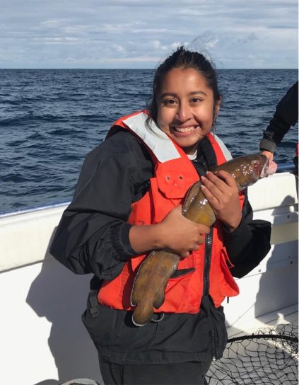 Ruhika Bhattacharya smiling in a boat holding a fish water in the background