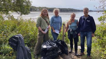 4 people smile for the camera with trash bags for a marine debris cleanup event. Water in the background.