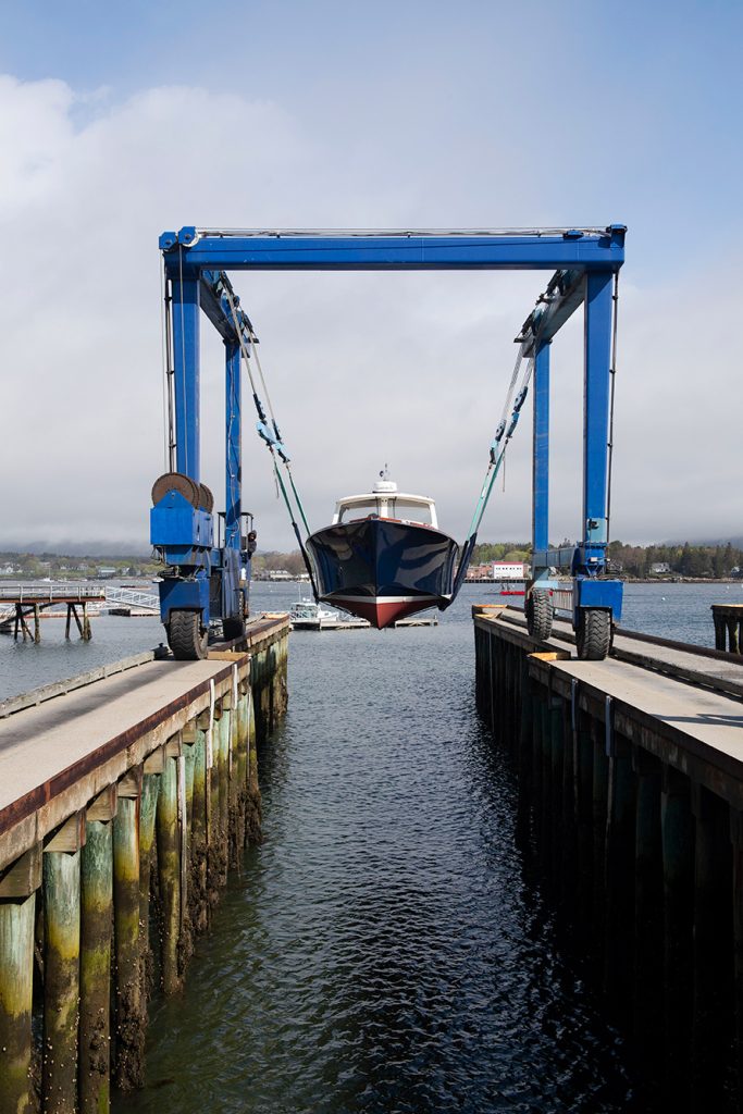 A yacht is lowered into the ocean between two long wooden piers.