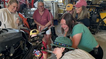 Several people giggle as they gather around an outboard engine together