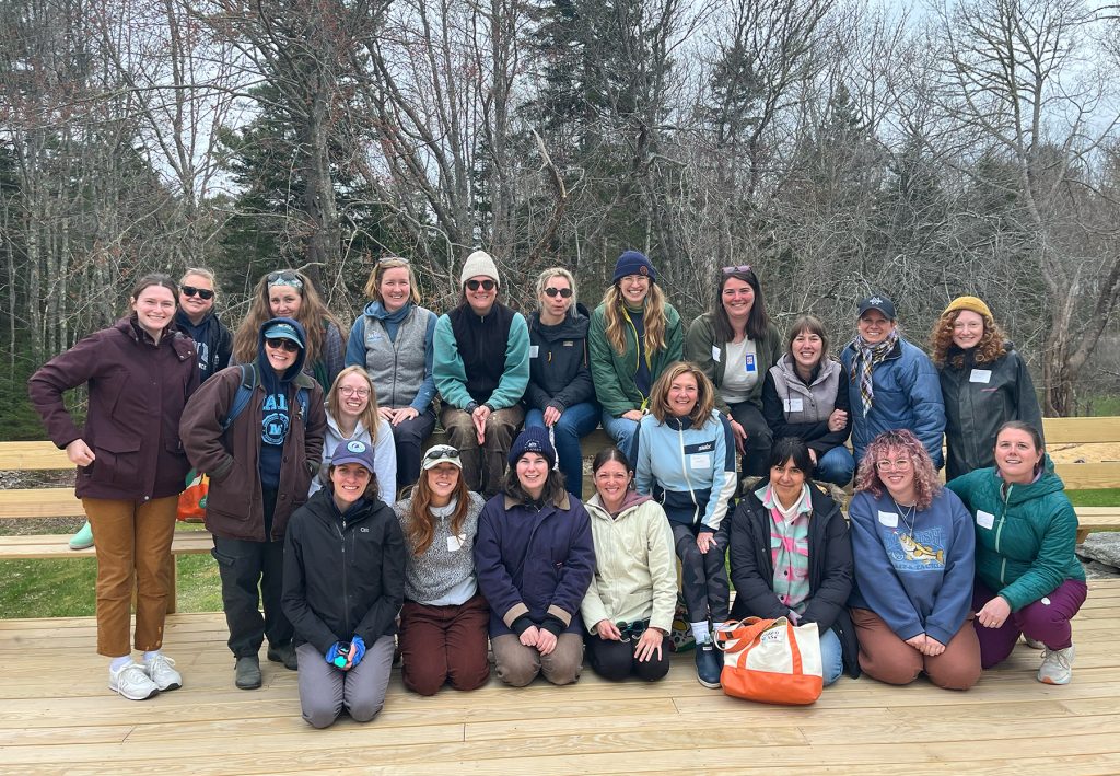 A large group of people pose smiling on a wooden platform