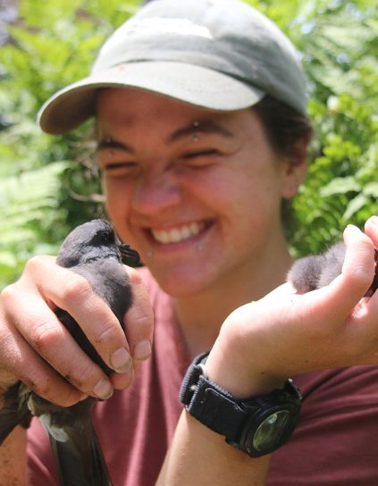 Autumn Pauley surrounded by greenery and holding two fledglings