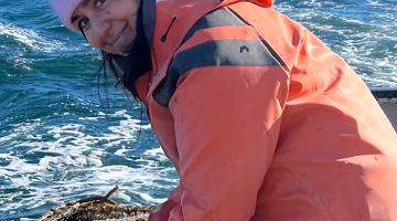 Michelle in a pink cap and orange jacket with the ocean behind her