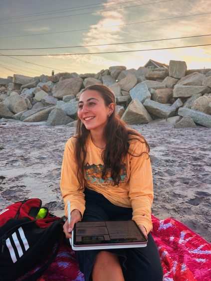 Olivia Ellis sitting on the beach at sunset.